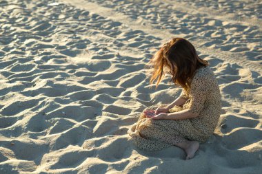 Sahilde oturan üzgün kız. Deniz kenarındaki güzel gün batımı. sahilde kum