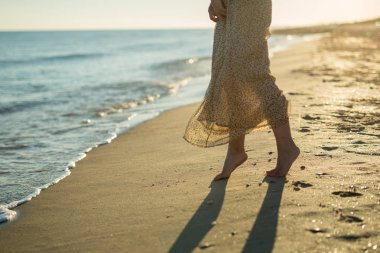 Kız sessizce sahilde kum üzerinde duruyor. Deniz kenarındaki güzel gün batımı.