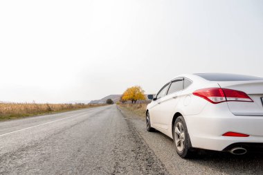 Beyaz araba sonbaharda yolun kenarında duruyor. Otomatik seyahat, otostop. Tatile dağlara gidelim.