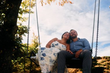 Dağlarda salıncakta sallanan bir çift, arka planda büyüleyici doğal manzarayla öpüşüyorlar. Seyahat, romantizm, yaşam tarzı ve macera temaları için mükemmel