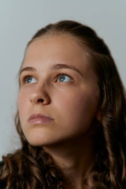 Kıvırcık saçlı, mavi gözlü, düşünceli ve umut dolu bir ifadeyle yukarı bakan genç bir kadının stüdyo portresi.