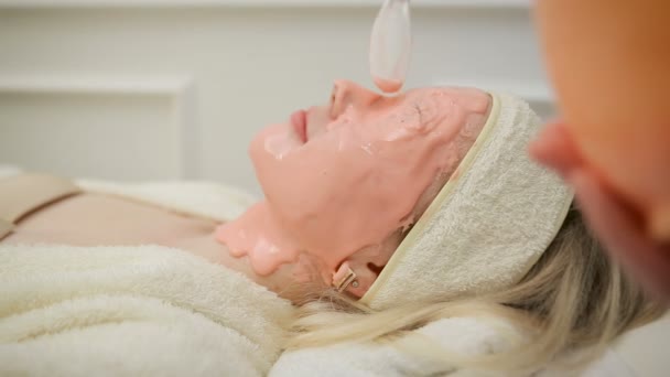 Una vista de cerca de la cara de las mujeres con máscara rosa. esteticista limpiando mascarilla facial. Pelar. Belleza y cuidado de la piel corporal . — Vídeos de Stock