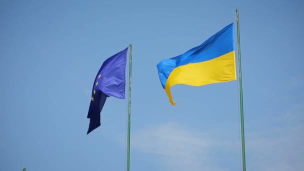 Bandera de Ucrania y bandera de la Unión Europea ondeando sobre un fondo de cielo azul — Vídeos de Stock