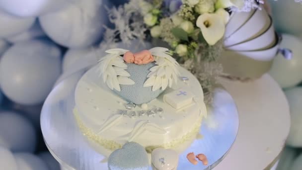 Tårta för dopet händelse med liten bibel och kors på vit glasyr och barnet docka på toppen av blå hjärtform och vita vingar form. Dopstårta för nyfödda barn — Stockvideo