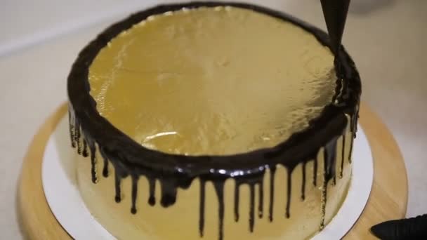 Шеф сжимает сливки. Шоколадная глазурь на золотом торте — стоковое видео