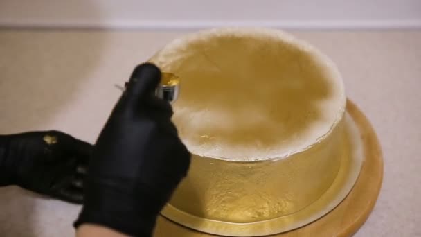 Pastelero cubre un pastel de una pistola de esmalte esmalte con recubrimiento brillante dorado. Las manos de los panaderos decoran el pastel — Vídeos de Stock