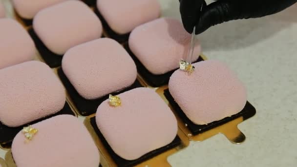 Confeiteiro adicionando um elemento de decoração de folha colorida de ouro comestível ao topo do bolo de mousse moderno com cobertura de veludo de cor rosa. Bolo de mousse de veludo quadrado elegante, recheio de nozes e frutas no interior — Vídeo de Stock