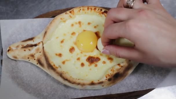 Şef el, khachapuri 'ye tereyağı ve yumurta sarısı koyar. Khachapuri 'ye yakın çekim: geleneksel Gürcistan ve Ermeni turtası, sulguni peynirli ve yumurtalı. Ekmek yerine servis edilmiş. Doğu yemekleri. Üst görünüm. — Stok video