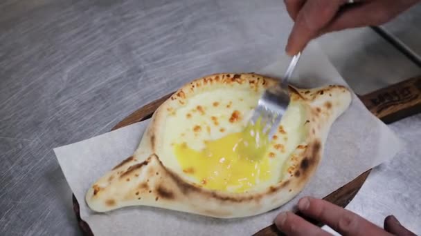 Hand mixing ingredients of adjarian khachapuri with fork in restaurant. Open bread pie with cheese and egg yolk. Yummy georgian cuisine. — Stock Video