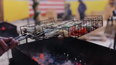 Şef açık mutfak restoranındaki ızgarada sebze pişiriyor. Izgara patates, mantar, kabak ve soğan pişir. Yemek hazırlama. Şef, içinde ızgara sebzeler olan metal ızgarayı çevirir.