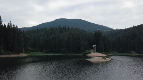 Voo de drone sobre o Lago Synevyr nas montanhas dos Cárpatos no dia ensolarado de verão. Bela natureza, lago cercado por floresta ao redor, belo lugar na Ucrânia — Vídeo de Stock