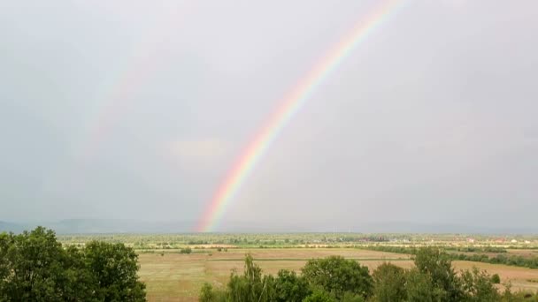 El lapso de tiempo de un arco iris contra un paisaje de montaña y un cielo nublado y lluvioso — Vídeos de Stock