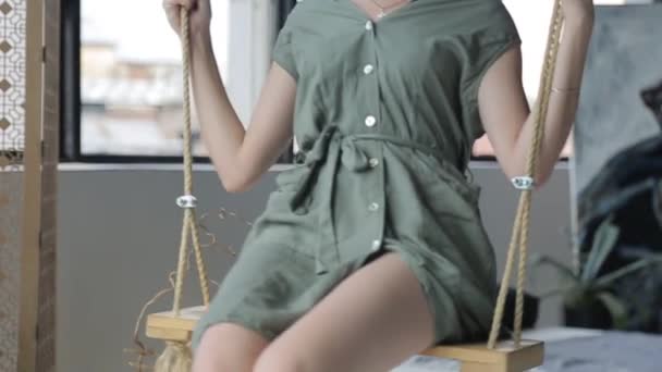 Chica joven en un vestido verde, montando un columpio en la habitación — Vídeos de Stock