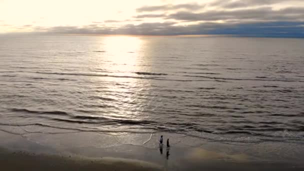 Dos personas están caminando por la playa. Vuela sobre el mar en un día soleado. El sol en el oeste se refleja en el agua — Vídeos de Stock