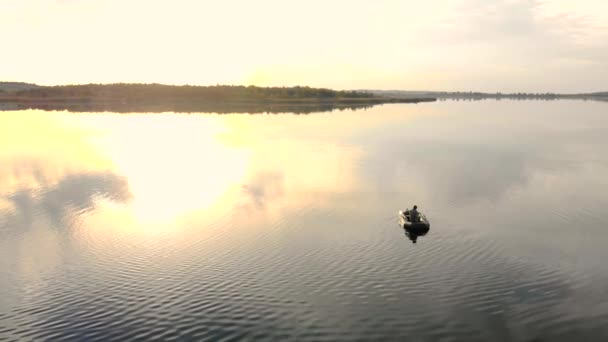 At sunset, the rays are reflected in the water the fisherman sits in the boat. — Stock Video