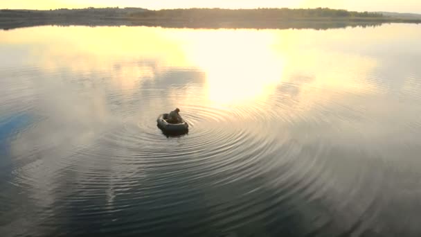 At sunset, the rays are reflected in the water the fisherman sits in the boat. — Stock Video