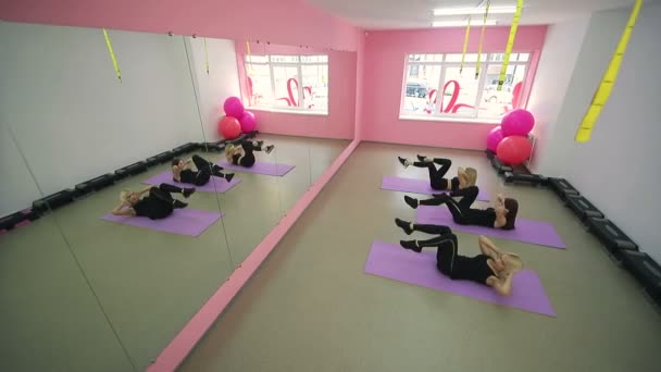 Grupp av sympatiska tjejer bedriver träning i gymmet. Liggande på mattan gör övningar med fötterna och pumpa pressen tittar sig i spegeln. — Stockvideo