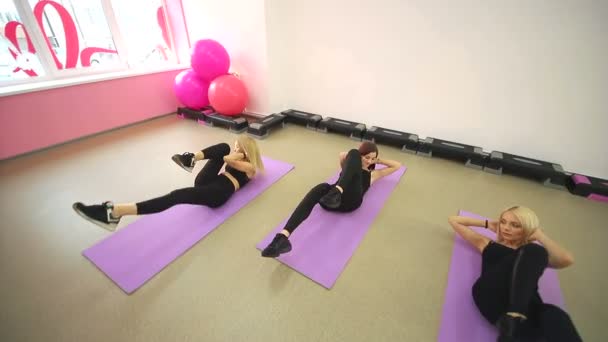 Szimpatikus lány csoport vesznek részt, az edzőteremben fitness. Feküdt a szőnyeg, gyakorolja a lábát, és pumpáló a sajtó nézi magát a tükörben. — Stock videók