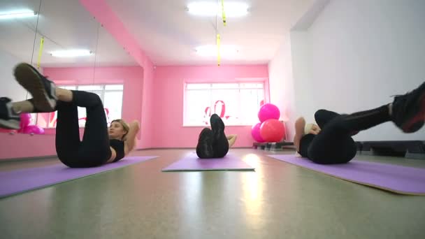 Grupo de chicas simpáticas se dedican a la aptitud en el gimnasio. Acostado en la alfombra haciendo ejercicios con sus pies y bombeando la prensa mirándose en el espejo . — Vídeos de Stock