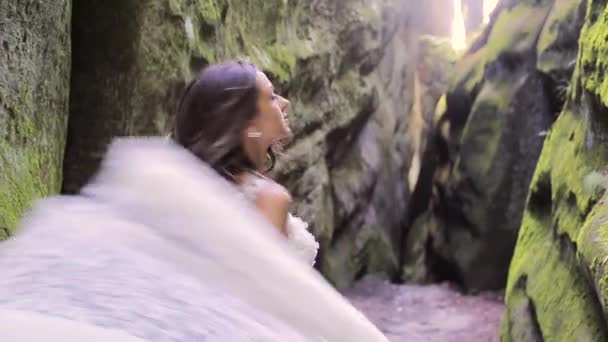 Мила наречена у весільній сукні біжить між каменями, і дивиться на камеру з великою посмішкою. Щасливі обличчя, емоції — стокове відео