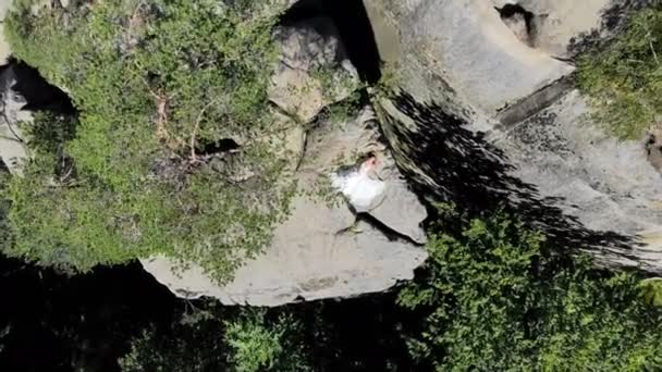 Aerial footage, bruden är på kanten av avgrunden. Höga klippor omger bruden. Kameran långsamt flyger och flyger bort från bruden — Stockvideo