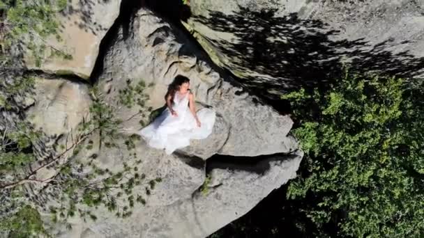 Luftaufnahmen zeigen, wie die Braut am Rande des Abgrunds steht. Hohe Klippen umgeben die Braut. die Kamera fliegt langsam von der Braut weg — Stockvideo