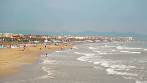 Timelapse spiaggia con i turisti che hanno un riposo, le onde arrivano rapidamente a riva. I vacanzieri camminano sulla sabbia gialla, camminando intorno al mare. Spiaggia di Valencia — Video Stock