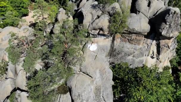 Luchtfoto beelden, bruid is aan de rand van de afgrond. De bruid wordt omgeven door hoge kliffen. De camera langzaam vliegt en vliegt weg van de bruid — Stockvideo