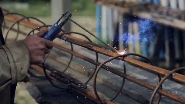 Um empregado solda uma estrutura metálica em um canteiro de obras. Obras de construção. Trabalho ao ar livre — Vídeo de Stock