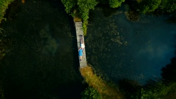 Luchtfoto bovenop. Twee geliefden van jongeren liggen op een houten brug. Sprookje rond een jong koppel. Gelukkige jonge paar. — Stockvideo