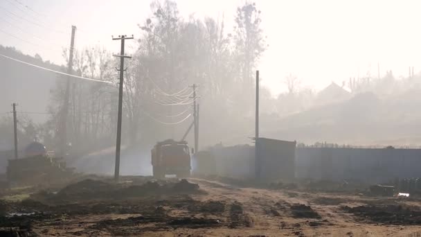 El camión se mueve a lo largo del sitio de construcción. Niebla matutina y humo alrededor . — Vídeos de Stock