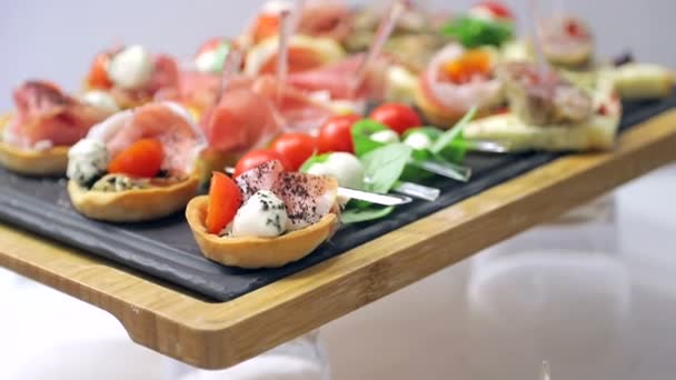 Feche os canapés de sanduíche na mesa do buffet. Tomates vermelhos com queijo mussarela com ervas e salsicha com pão — Vídeo de Stock