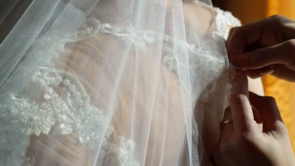 Frauen drücken Knöpfe in Großaufnahme an einem Hochzeitskleid. ein Hochzeitstag, die Sonnenstrahlen fallen auf den Rücken der Bräute — Stockvideo