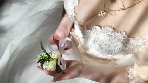 Panna Młoda w ręku trzyma kwiat Boutonniere i pokazuje go. Promienie słoneczne wchodzą na ciało narzeczonych i kwiat — Wideo stockowe