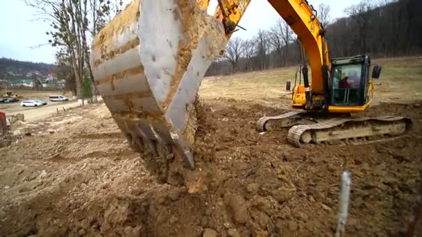 Повільний рух копанця копає яму і кидає бруд. Крупним планом відро екскаватора, що викидає землю. Знімок під широким кутом об'єктива — стокове відео