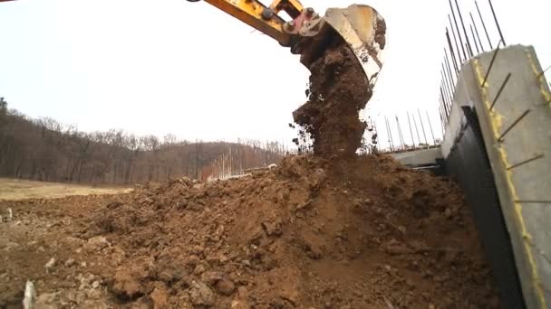 Movimiento lento de una excavadora cavando un hoyo y arrojando tierra. Primer plano de un cubo de excavadora que arroja la tierra. Disparo con lente gran angular — Vídeo de stock