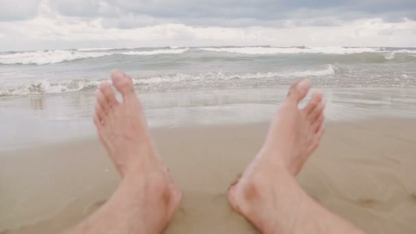 Nahaufnahme von Männerfüßen am Strand. Ein Blick auf die Meereswellen, die ans Ufer kommen. Sommerferien. — Stockvideo