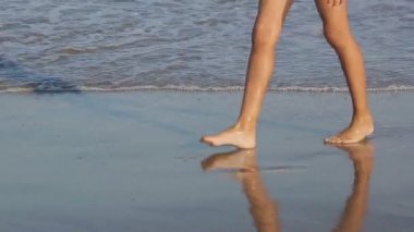 Bir kız Sahilde yürüyüş çocuk bacakları close-up. Denizi çevresinde yürüyüş. Kıyıya gelen dalgalar deniz bir bakış. Yaz tatil tatil.