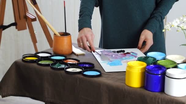 La mano femenina del artista, mezcla los colores en el tablero, y se prepara para pintar un cuadro con pinturas acrílicas — Vídeo de stock