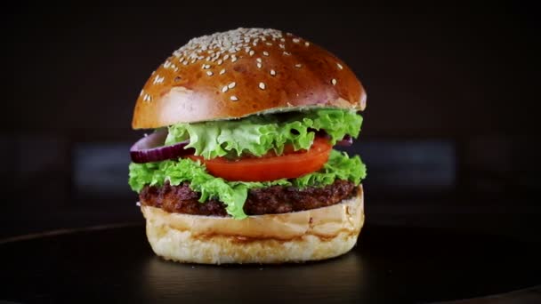 Hamburguesa con chuleta gira sobre un tablero de madera sobre un fondo negro . — Vídeo de stock