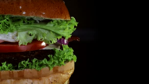 Burger, avec une escalope et des œufs brouillés recouverts de légumes verts tourne sur une planche en bois. Du fond noir . — Video