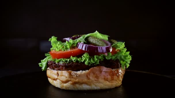 O pão cai sobre o hambúrguer em câmara lenta. Comida rápida. Delicioso hambúrguer no fundo preto — Vídeo de Stock