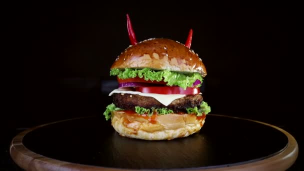 Fast Food. Burger mit rotem Pfeffer, der sich langsam auf einem Holzbrett auf schwarzem Hintergrund dreht — Stockvideo