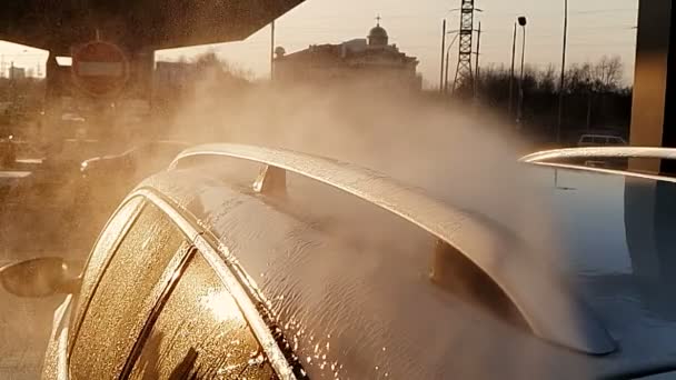 Car wash super slow motion. Splashes of water are broken about the car. The sun at sunset shines into the chamber, and illuminates the particles of water. — Stock Video