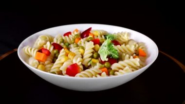 Bir plaka üzerinde sebze ile spiral makarna siyah bir arka planda döner. Yeşil karnabahar bir plaka üzerinde düşüyor