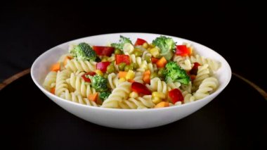 Bir plaka üzerinde sebze ile spiral makarna siyah bir arka planda döner