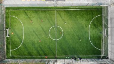 Yapay çim ile yeni bir alanda futbol oynayan bir grup çocuk