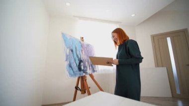 Kadın ressam bir spatula ve akrilik boyalarla resim yapmaya başlar. Tablo üzerinde bir çizim oluşturuluyor
