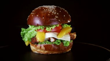 Et, yeşillik ve peynir büyük bir parça ile Burger siyah arka planda ahşap bir tahta üzerinde dönüyor