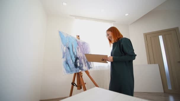 Mujer artista comienza a pintar un cuadro con una espátula y pinturas acrílicas. Crear un dibujo sobre lienzo — Vídeo de stock